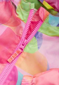 Veste de pluie colorée avec une finition brillante. Elle possède une fermeture éclair rose et des motifs abstraits pastel en rose, vert et bleu. Manches élastiques incluses.