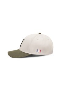 Krém színű baseball sapka olívazöld napellenzővel. Elöl hímzett logó található, az oldalon pedig három színes csík (piros, fehér, kék) van.
