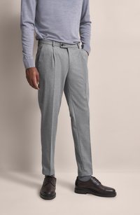 Graue, gefaltete Hose aus strukturiertem Stoff, mit seitlichen Taschen und Knopfverschluss, kombiniert mit dunklen Lederschuhen.