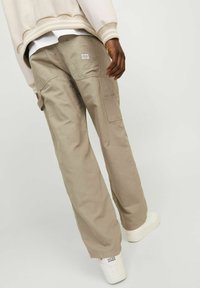 Pantalones cargo beige con bolsillos laterales y un ajuste relajado. El material parece ligero y duradero. Combinados con zapatillas blancas.