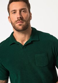 Polo verde realizzato in tessuto morbido, con colletto classico, maniche corte e taschino sul petto. Texture liscia con un colore uniforme.