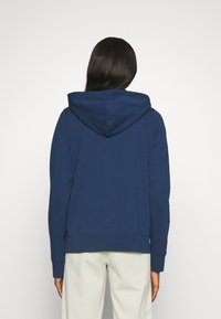 Sudadera azul marino con bolsillo tipo canguro, capucha ajustable y puños acanalados. Textura suave, corte casual y diseño minimalista.