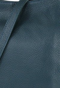 Donkerblauwe handtas van getextureerd leer met een gladde afwerking en stevige bandjes, voorzien van een subtiel korrelpatroon en nette randen.