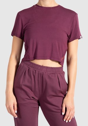 Woman wearing matching dark purple cropped t-shirt and elastic waist pants against a plain background.