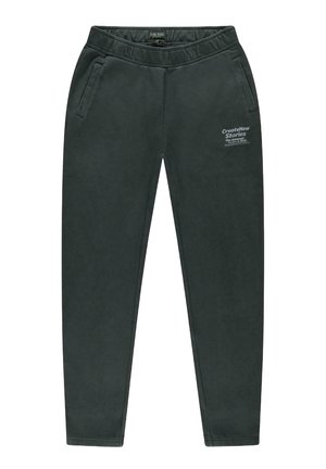 Donkergroene trainingsbroek van zacht materiaal, met zijzakken en een elastische tailleband, met een gedrukt tekstdetail op de linker dij.