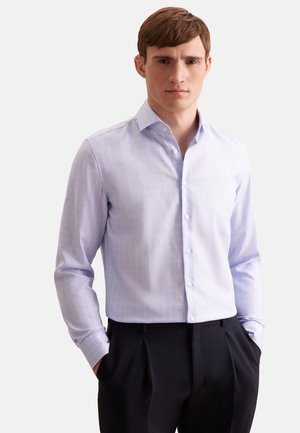 Camicia azzurra con bottoni, caratterizzata da un leggero motivo a quadri. Presenta un colletto classico e maniche lunghe, realizzata in tessuto morbido. Abbinata a pantaloni scuri.