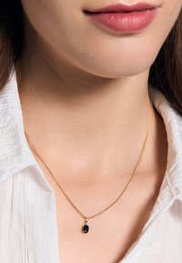 Złocona naszyjnik wielowarstwowy z owalnym czarnym wisiorkiem. Łańcuszki są cienkie i delikatne, uzupełniając minimalistyczny design.