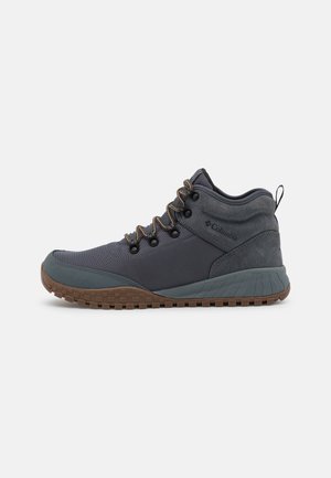 Scarpa da trekking Columbia grigio scuro con lacci marroni, suola marrone robusta e supporto imbottito per la caviglia, mostrata di profilo su sfondo bianco.