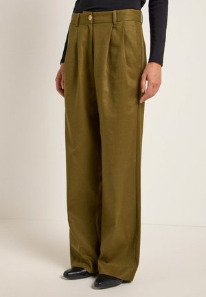 Hose mit weitem Bein aus olivgrünem Stoff, mit Falten, Knopfverschluss und glatter Textur; kombiniert mit schwarzen Schuhen.