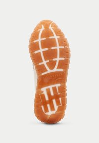Sula på en sneaker, med ett gripmönster i orange gummi och vita accenter. Texturerad yta för grepp, med varumärkesnamnet präglat.