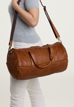 Brown leather duffel bag with dual handles and a detachable shoulder strap. Soft texture, rounded shape, and accent stitching detail.