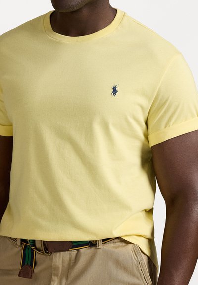 Yellow cotton t-shirt with a crew neck, short sleeves, and a blue embroidered logo on the left chest. Worn with a green and yellow striped belt.