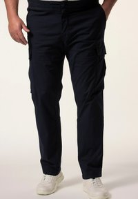 Námořnické modré cargo kalhoty vyrobené z lehkého materiálu, s několika bočními kapsami a rovnými nohavicemi. Nosené s bílými teniskami.