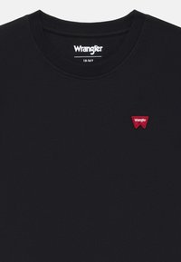 Melnas kokvilnas T-krekls ar apaļu kakla izgriezumu, uz kreisās puses ar mazu sarkanu izšuvumu Wrangler logo. Vienkāršs dizains, gluda tekstūra.
