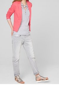 Blusa grigia chiara con scollo henley, abbinata a un blazer corallo. I pantaloni grigi chiari e i sandali metallici argentati con cinghie completano il look.