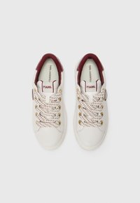 Baskets en cuir blanc avec des accents bordeaux, des œillets dorés et des lacets à motifs. Texture lisse avec un design à bout arrondi.