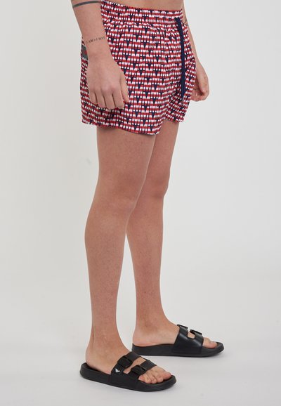 Costumi da bagno a righe rosse e bianche con vita elastica e cordoncino, abbinati a sandali neri con due fascette regolabili.