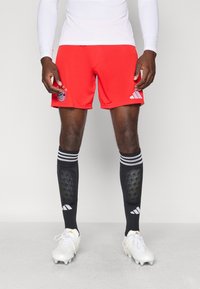 Röda träningsshorts med logodetalj, kombinerat med svarta kompressionssockor med vita ränder och vita fotbollsskor med silverdetaljer.