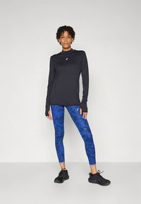 Juoda ilgomis rankovėmis sportinė palaidinė su aukštu kaklu, derinama su mėlynos spalvos raštuotomis tamprėmis. Juodi sportbačiai užbaigia įvaizdį.