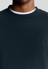 Felpa verde scuro con un tessuto testurizzato, caratterizzata da un collo a giro e un logo ricamato sul petto. Design semplice e versatile.
