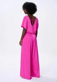 Fuksjowy kombinezon z krótkimi rękawami, szerokimi nogawkami i dekoltem w kształcie łezki z tyłu. Gładki, lekki materiał z płynącym krojem.