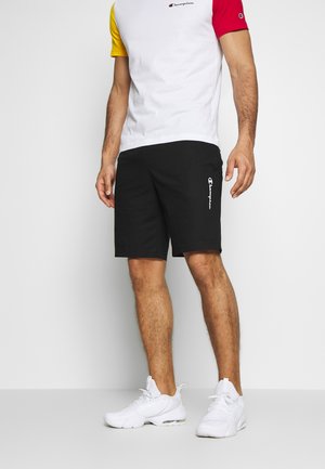 Czarne szorty z bocznymi kieszeniami i białym logo, w zestawieniu z wielokolorową koszulą z krótkim rękawem, z żółtymi, czerwonymi i białymi sekcjami. Białe buty.