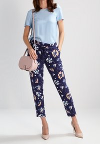 Světle modrý top s krátkým rukávem v kombinaci s námořnickými květinovými kalhotami. Světle růžová kabelka přes rameno a béžové podpatky dokončují vzhled.