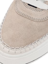 Close-up of beige suede sneaker toe with white braided stitching, white sole, and white shoelace partially visible.