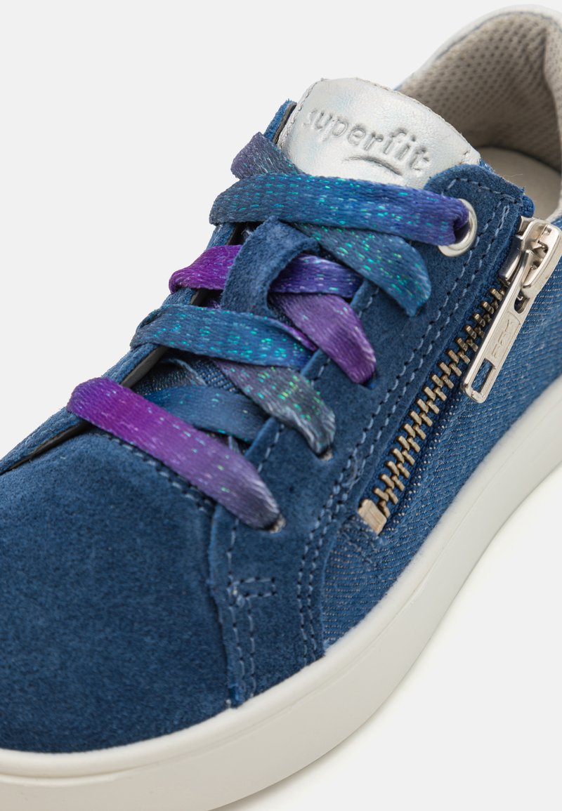 Blaue Wildledersneaker mit metallic-silbernem Logo, mehrfarbigen Schnürsenkeln, seitlichem Reißverschluss und einer weißen Gummisohle. Glatte Textur und lässiges Design.