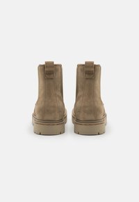 Botas de tobillo de ante marrón con un acabado texturizado, diseñadas con una lengüeta y una suela de goma ligera. La vista trasera muestra la forma y la costura.