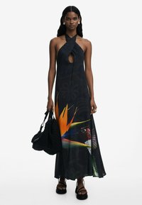Black maxi dress with a keyhole design, featuring vibrant floral graphics and a loose fit. Model holds a black bag with intricate texture.