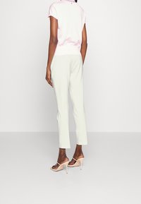 Jasnoróżowa bluzka z krótkim rękawem z marszczonym pasem. Miękkie zielone spodnie o prostym kroju. Modelka ma na sobie beżowe sandały na wysokim obcasie.