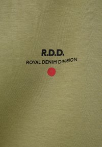 Olivovo zelená tkanina s čiernym textom "R.D.D. ROYAL DENIM DIVISION" nad malou červenou bodkou v strede.