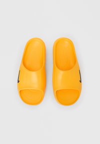 Par af lyse orange slip-on sandaler med åbne tæer og sorte swoosh-logoer på en hvid baggrund.