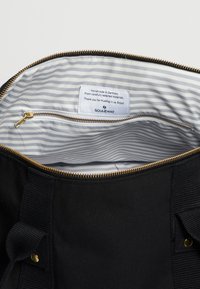 Černá plátěná taška uvnitř se zlatým zipem. Podšitá světle šedou a bílou pruhovanou tkaninou. Štítek říká "Ručně vyrobeno v Německu."