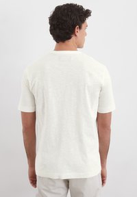 Weißes T-Shirt mit kurzen Ärmeln und strukturiertem Finish. Rundhalsausschnitt und kleines Etikett am Rücken, das von hinten sichtbar ist.