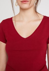 Burgundy fitted t-shirt with a v-neck, short sleeves, and smooth cotton texture. Detail stitching along the neckline.