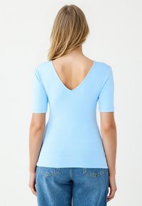 Lichtblauw kortemouwen top met een V-hals achterkant, gemaakt van een gladde stof, gecombineerd met high-waisted denim jeans.
