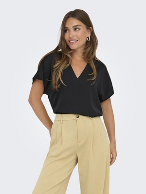 Black V-neck top with short sleeves paired with beige high-waisted, pleated trousers. Soft fabric, relaxed fit, minimal design.