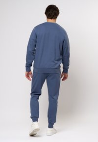 Modra majica s kapuco in ujemajoče se hlače iz mehkega materiala. Obleka ima sproščen kroj, rebraste manšete in preprost dizajn.