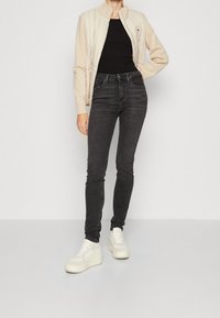 Chaqueta acolchada beige sobre una blusa negra ajustada, combinada con jeans oscuros ajustados y zapatillas de plataforma blancas. Texturas de tejido lisas.