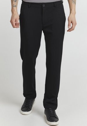 Black trousers made of soft, smooth fabric, featuring a straight-leg cut, button closure, and side pockets. Worn with black sneakers.