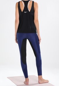 Débardeur de sport noir avec dos ouvert et logo blanc, associé à un legging bleu et noir présentant des motifs en blocs de couleurs courbés.