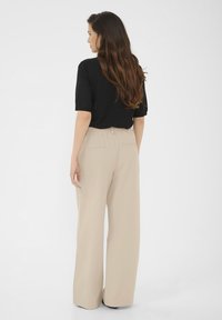 Haut noir à manches courtes associé à un pantalon large beige. Le pantalon a une taille élastique et deux poches arrière. Tissu lisse et léger.