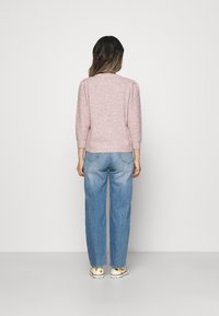 Różowy sweter o fakturze z rękawami do łokcia, w połączeniu z jasnoniebieskimi jeansami o szerokich nogawkach i wzorzystymi trampkami, widziany od tyłu.