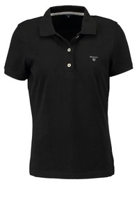 Černé polo tričko vyrobené z bavlny, s plochým límečkem, třemi knoflíkovými zapínáními a malým vyšitým logem na hrudi. Krátké rukávy.