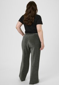 Šedé, třpytivé kalhoty širokého střihu s elastickým pasem, spárované s jednoduchým černým tričkem s krátkým rukávem, pohled ze zadu.