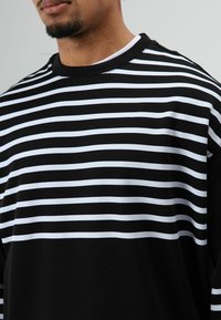 Zwart-witte gestreepte trui met horizontale strepen, een ronde hals, zachte textuur en een ontspannen pasvorm. Gedetailleerd met contrasterende kleuren.