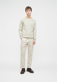 Maglione lavorato a maglia grigio chiaro a maniche lunghe, pantaloni crema e scarpe in pelle marrone scuro. Design minimalista con vestibilità rilassata.