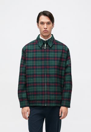 Veste à carreaux verte et bleu marine avec des accents rouges, dotée d'un col, d'une fermeture éclair à l'avant et de manches longues. Tissu texturé avec une coupe décontractée.